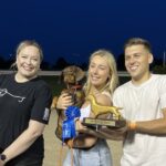 two woman and a man pose with the first place ribbon, trophy and wiener dog winner