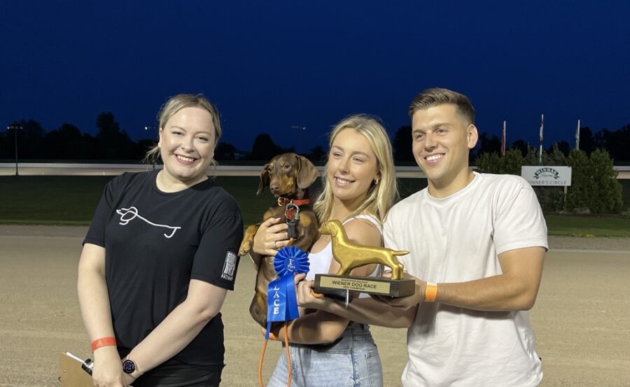 two woman and a man pose with the first place ribbon, trophy and wiener dog winner