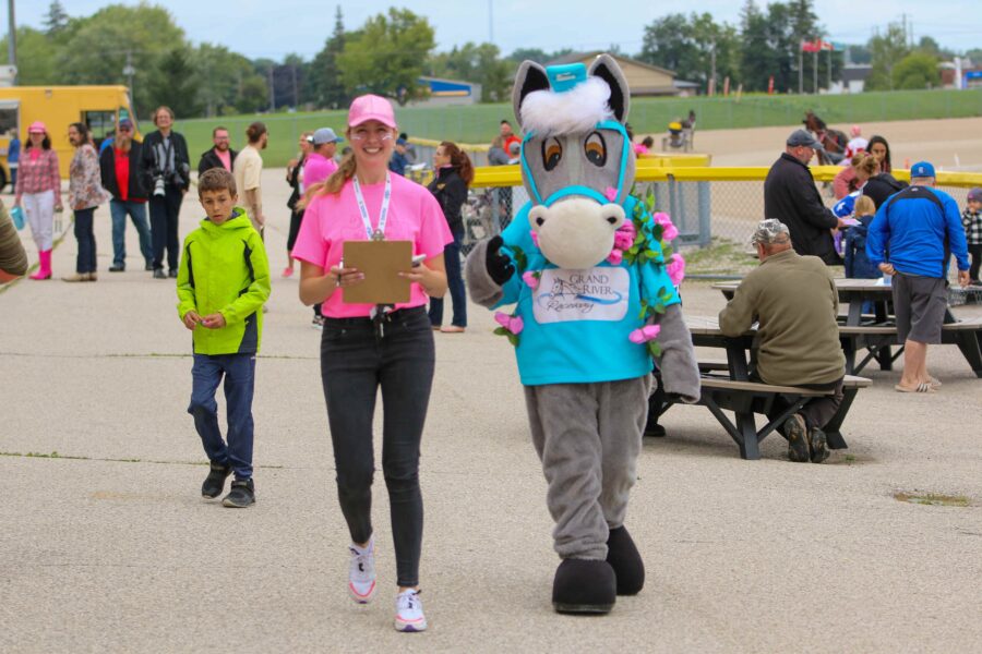 woman in pink tshirt next to horse mascot Grandy in blue tshirt and pink flowers around its neck